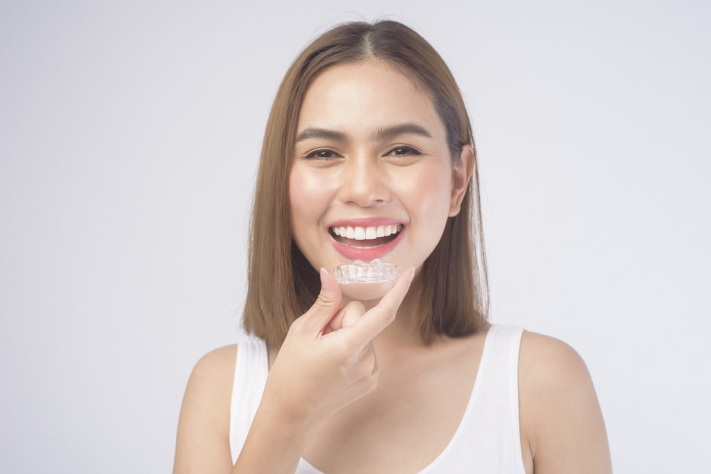 Woman smiles while holding Invisalign, not mail-in aligners